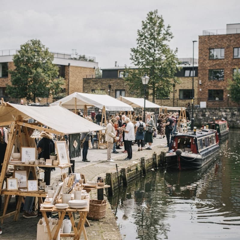 Market stalls along a canal with narrowboats moored beside them.
